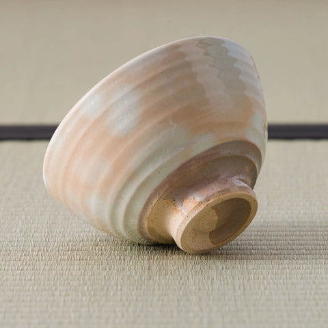 Chawan tipped on its side to show the carved foot ring and layered bands of peach and cream glaze.