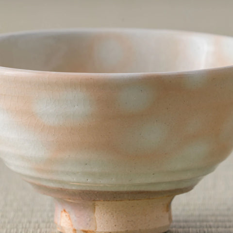 Close-up of the rim and side of a spotted peach-glazed chawan showing gentle throwing ridges.