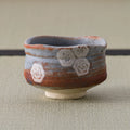 Nezumi Shino chawan with grey-blue glaze over rust tones and stamped hexagonal blossom motifs.