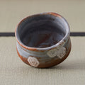 Angled view of a Nezumi Shino chawan showing its interior and hexagon flower stamps near the rim.