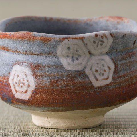 Close-up of hexagonal blossom motifs over warm rust and grey Shino glaze on a chawan.