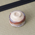 Shino chawan turned upside down, showing its carved white clay foot ring and layered grey and rust glaze.