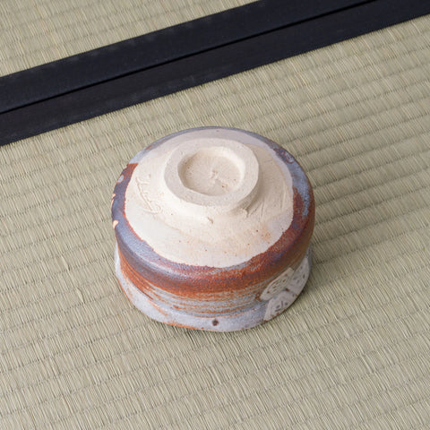 Shino chawan turned upside down, showing its carved white clay foot ring and layered grey and rust glaze.