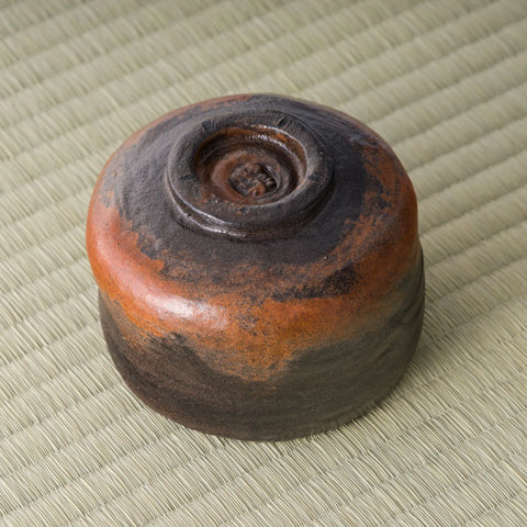 Kuro-raku black raku matcha bowl, underside view showing the foot and orange firing marks