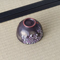 Black Weeping Sakura Chawan inverted on tatami, showing its russet unglazed foot ring and a red stamped seal