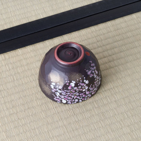 Black Weeping Sakura Chawan inverted on tatami, showing its russet unglazed foot ring and a red stamped seal