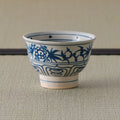 Blue-and-white porcelain bowl with blue floral decoration, side view on a tatami mat.