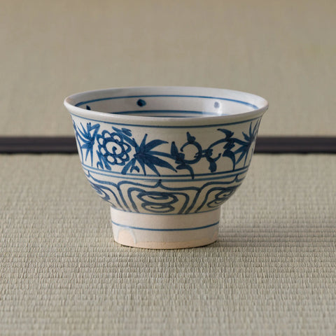 Blue-and-white porcelain bowl with blue floral decoration, side view on a tatami mat.