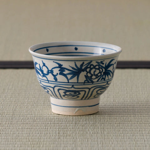 Blue-and-white porcelain bowl with floral scroll design, side view on a tatami mat.