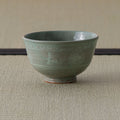 Grey-green celadon tea bowl, side view on a tatami mat.