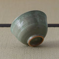 Grey-green celadon tea bowl tipped on its side, showing inlaid floral decoration and foot.