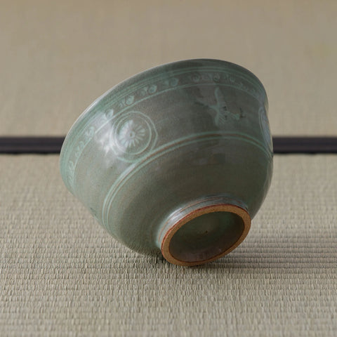 Grey-green celadon tea bowl tipped on its side, showing inlaid floral decoration and foot.