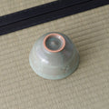 Grey-green celadon tea bowl inverted to show its foot ring, on a tatami mat.