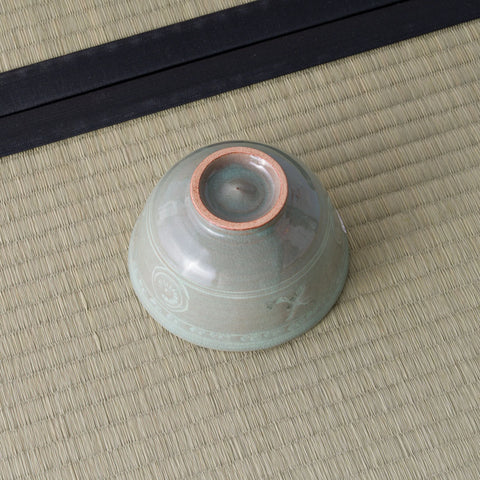 Grey-green celadon tea bowl inverted to show its foot ring, on a tatami mat.