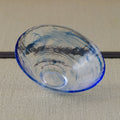 Pale blue glass tea bowl, three-quarter view showing the brushstroke design inside.