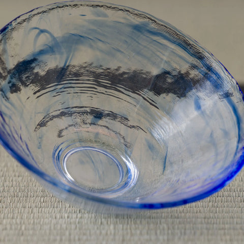 Pale blue glass tea bowl with a dark sumi-e brushstroke band, tilted to show the foot.