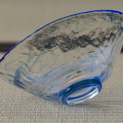 Pale blue glass tea bowl with a grey brushstroke band, tilted side view.