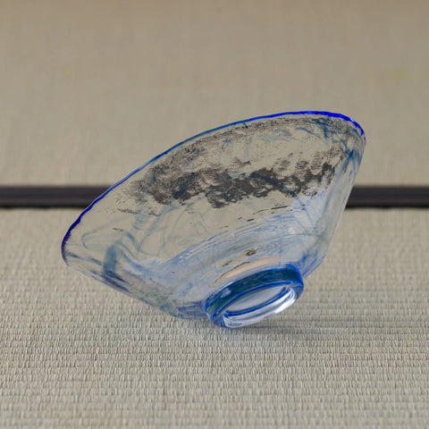 Pale blue glass tea bowl tipped on its side, brushstroke band and foot visible.