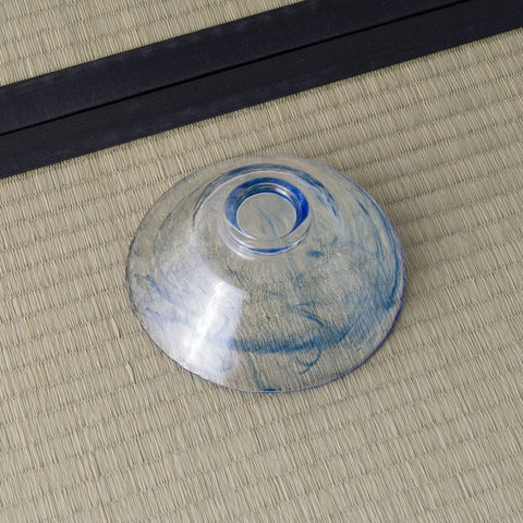 Pale blue glass tea bowl inverted to show its base, on a tatami mat.