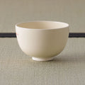 Cream tea bowl shown from its plain side, side view on a tatami mat.