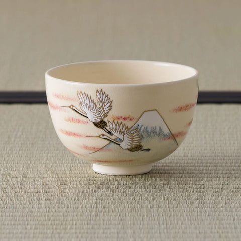 Cream tea bowl painted with cranes and Mount Fuji, side view on a tatami mat.