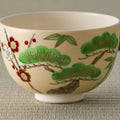 Cream tea bowl painted with pine, bamboo and red-and-white plum blossoms, front view.