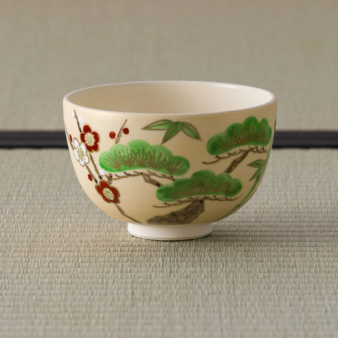 Cream tea bowl painted with pine, bamboo and red-and-white plum (shochikubai), side view.
