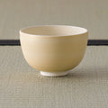 Plain cream-beige tea bowl, side view on a tatami mat.