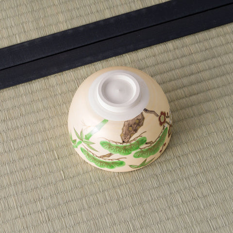 Cream bowl inverted to show its foot, painted with green pine and a brown branch.