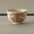 Cream tea bowl with a gold rim, painted with bamboo and red-and-blue flowers, side view.