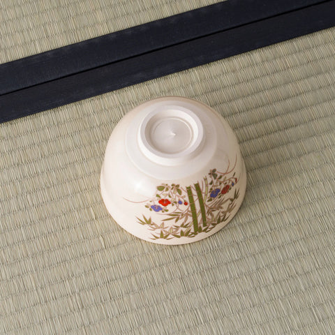 White bowl inverted to show its foot, with a small bamboo-and-flower sprig near the base.