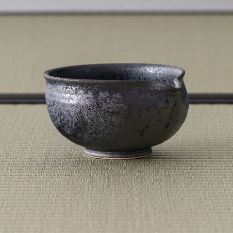 Three-quarter view of the dark chawan showing the spout-like pouring lip