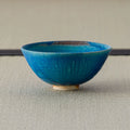 Deep teal glazed tea bowl, side view on a tatami mat.