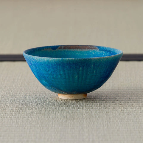 Deep teal glazed tea bowl, side view on a tatami mat.