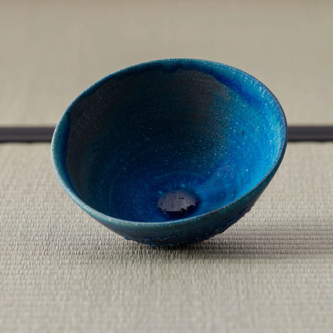 Deep blue glazed tea bowl, three-quarter view showing the interior, on a tatami mat.