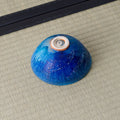 Deep blue glazed tea bowl inverted to show its spiral foot, on a tatami mat.