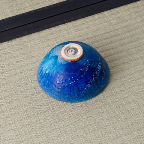 Deep blue glazed tea bowl inverted to show its spiral foot, on a tatami mat.
