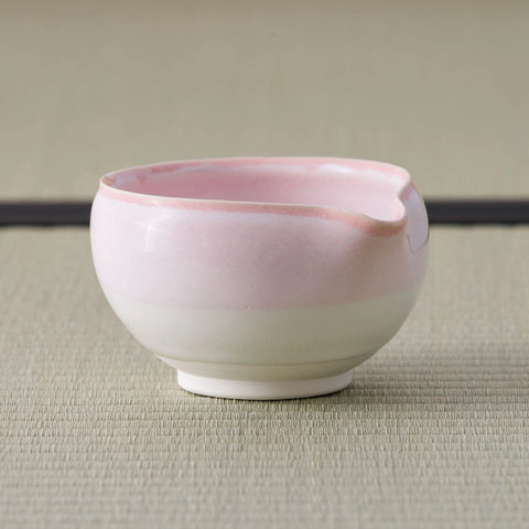 Tea bowl glazed pink at the rim fading to white at the base, side view on a tatami mat.