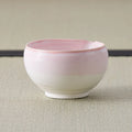 Tea bowl glazed pink at the rim fading to white below, side view on a tatami mat.