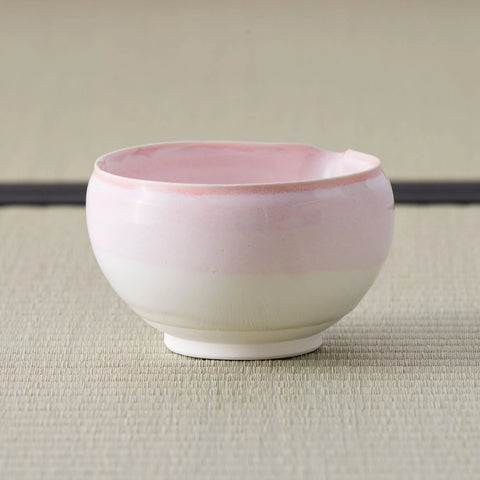 Tea bowl glazed pink at the rim fading to white below, side view on a tatami mat.
