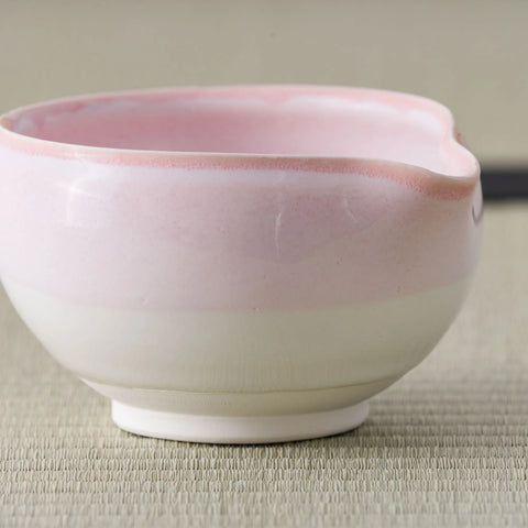 Tea bowl glazed pink fading to white with a lipped rim, side view on a tatami mat.