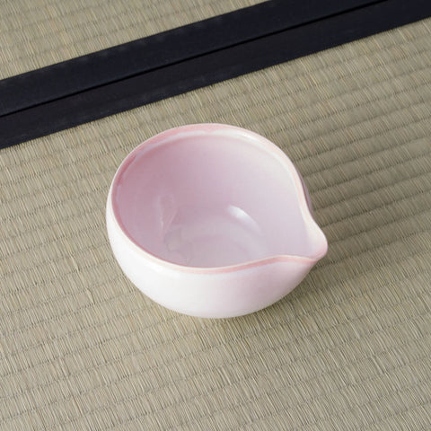 Pink-to-white glazed spouted bowl (katakuchi) viewed from above, showing the lip, on a tatami mat.