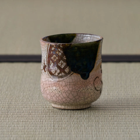 Pink crackle-glazed ceramic teacup with floral design, three-quarter view on a tatami mat.