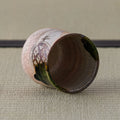 Pink crackle-glazed ceramic teacup tipped on its side to show the interior, on a tatami mat.