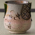 Close view of a pink crackle-glazed teacup with a brown stencil-floral design and a green glaze drip at the rim.