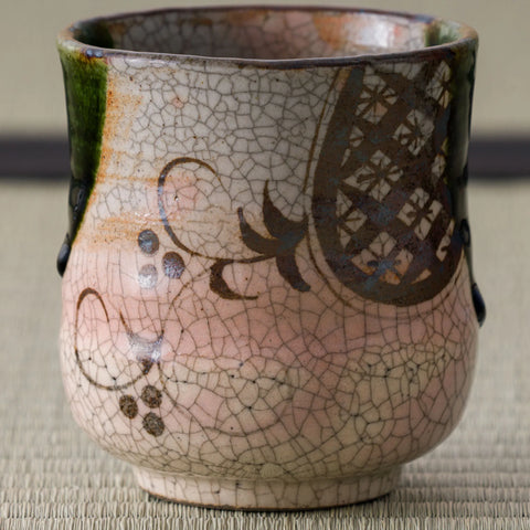 Close view of a pink crackle-glazed teacup with a brown stencil-floral design and a green glaze drip at the rim.