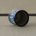 Blue-and-white striped teacup tipped on its side showing the dark interior, on a tatami mat.