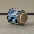 Blue-and-white striped teacup tipped over to reveal its unglazed foot, on a tatami mat.