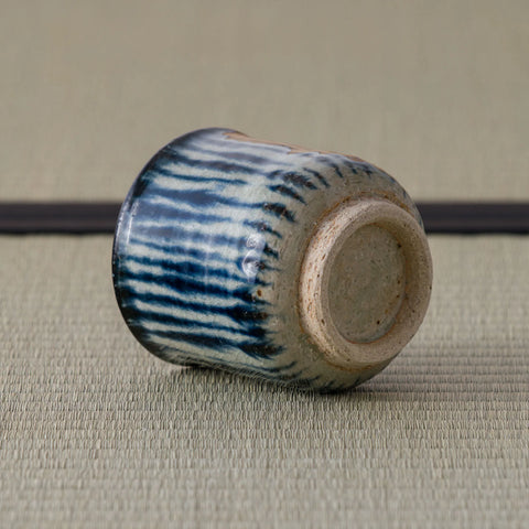 Blue-and-white striped teacup tipped over to reveal its unglazed foot, on a tatami mat.