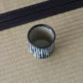 Blue-and-white striped teacup tilted to show its interior, on a tatami mat.